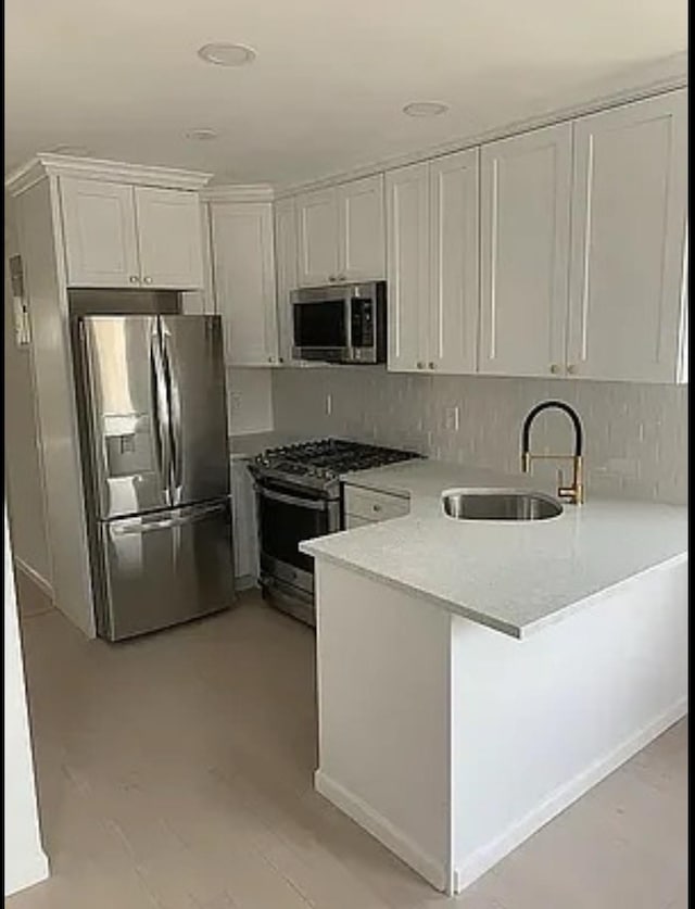 kitchen featuring kitchen peninsula, appliances with stainless steel finishes, decorative backsplash, sink, and white cabinetry