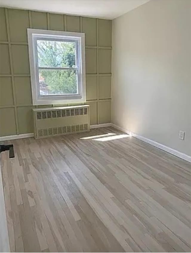 spare room with radiator heating unit and light hardwood / wood-style floors