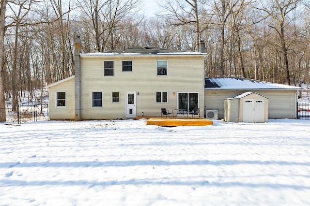 snow covered back of property with a storage unit and a wooden deck