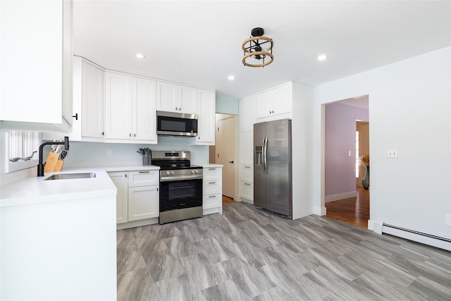 kitchen featuring white cabinetry, sink, stainless steel appliances, a baseboard radiator, and light wood-type flooring