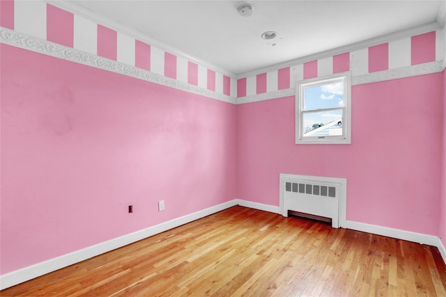 empty room with radiator heating unit, hardwood / wood-style flooring, and crown molding