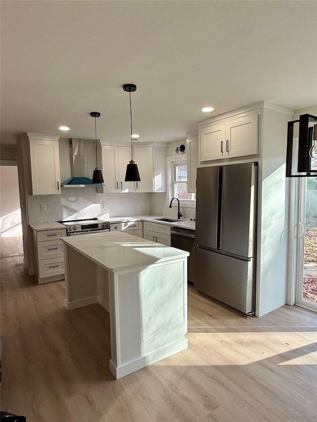 kitchen with white cabinets, wall chimney range hood, decorative light fixtures, a kitchen island, and stainless steel appliances