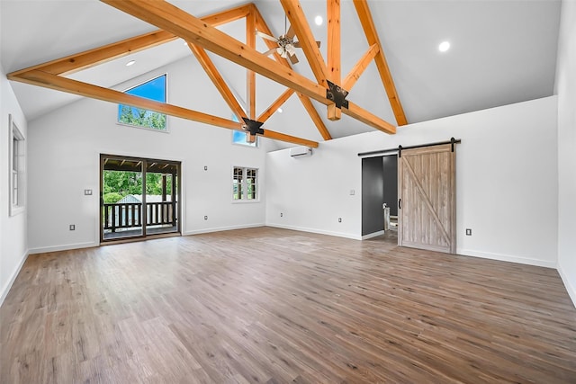 unfurnished living room with a barn door, beamed ceiling, high vaulted ceiling, a wall unit AC, and hardwood / wood-style floors