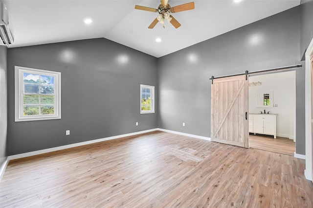 unfurnished bedroom with ceiling fan, sink, a barn door, lofted ceiling, and light wood-type flooring