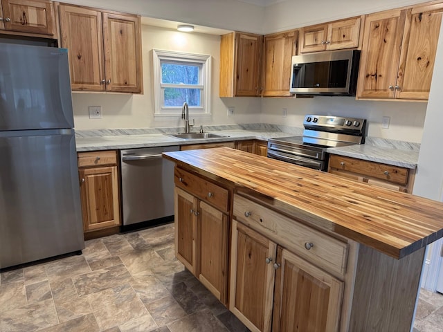 kitchen with a kitchen bar, appliances with stainless steel finishes, sink, a center island, and butcher block counters