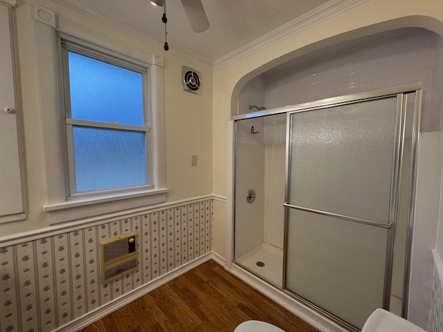 bathroom with ornamental molding, heating unit, ceiling fan, wood-type flooring, and a shower with shower door