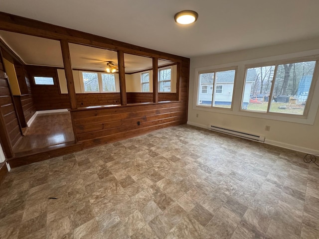 spare room featuring baseboard heating, wooden walls, and ceiling fan