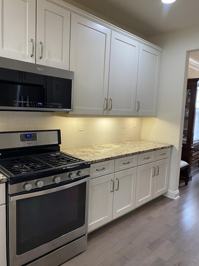 kitchen with light stone countertops, appliances with stainless steel finishes, backsplash, light hardwood / wood-style flooring, and white cabinets