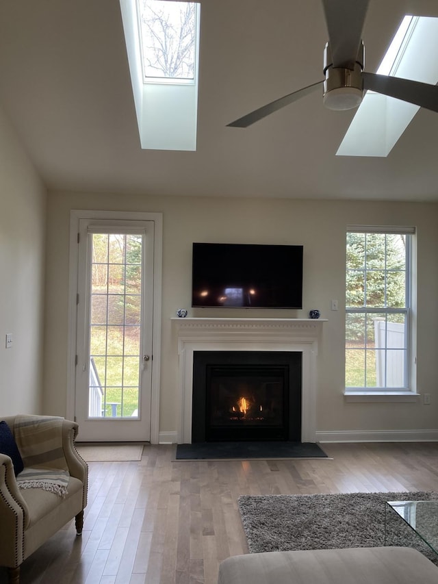 living room with ceiling fan, light wood-type flooring, a wealth of natural light, and a skylight