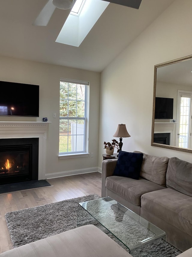 living room with ceiling fan, vaulted ceiling with skylight, a healthy amount of sunlight, and light hardwood / wood-style flooring