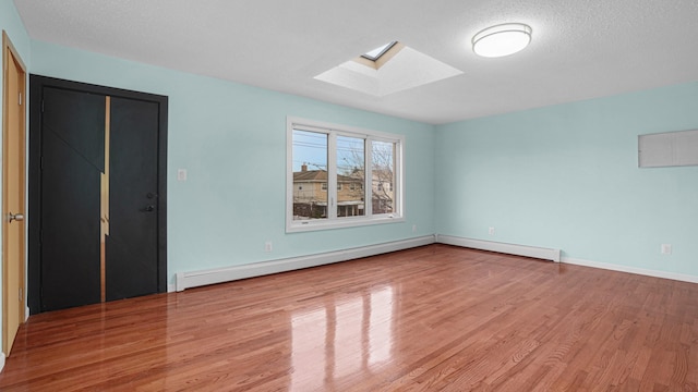 empty room with a textured ceiling, a skylight, baseboard heating, and light hardwood / wood-style flooring