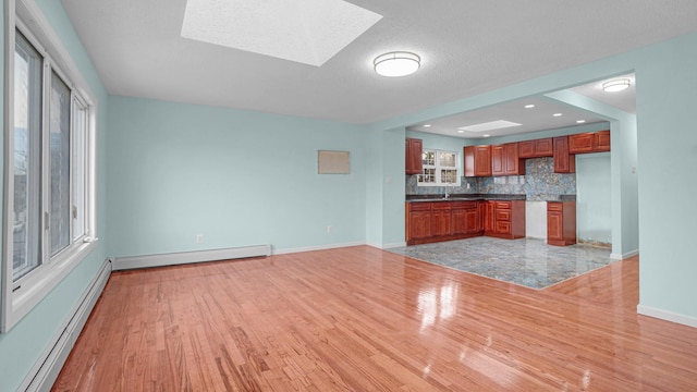 kitchen featuring a skylight, light hardwood / wood-style flooring, tasteful backsplash, and a baseboard heating unit