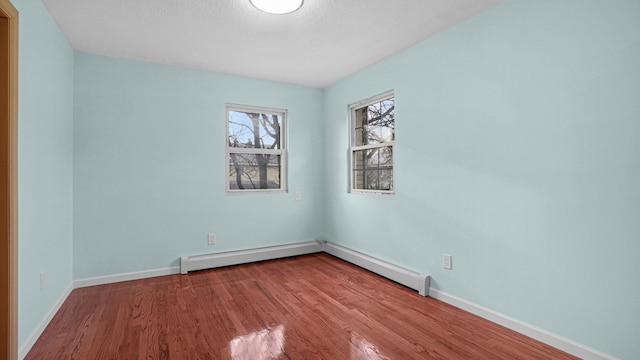 empty room with wood-type flooring and a baseboard heating unit