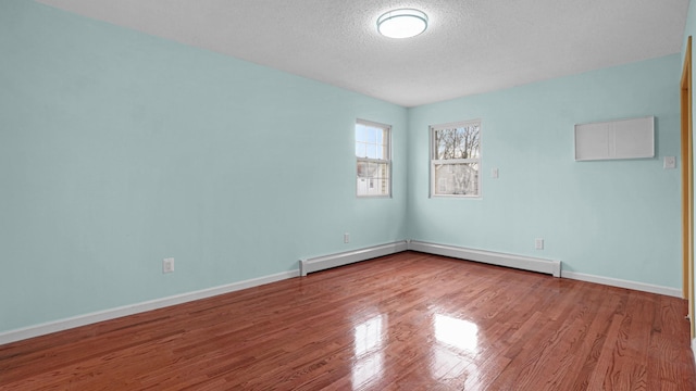 empty room featuring hardwood / wood-style floors, a textured ceiling, and a baseboard heating unit