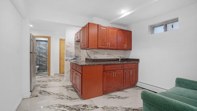 kitchen with decorative backsplash, dark stone counters, a baseboard heating unit, sink, and stainless steel refrigerator