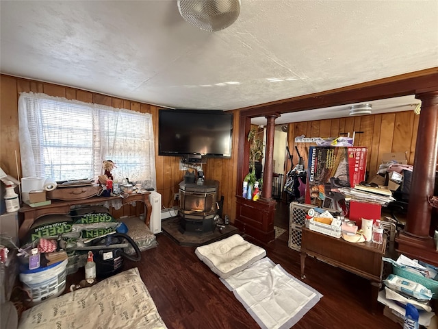 living room with dark hardwood / wood-style flooring, decorative columns, a textured ceiling, a wood stove, and wood walls