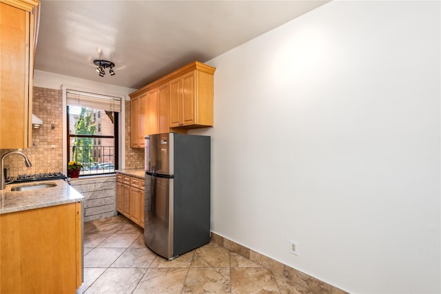 kitchen with tasteful backsplash, stainless steel fridge, light stone countertops, and sink