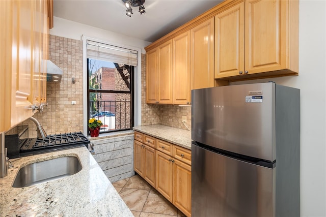 kitchen featuring sink, backsplash, light stone countertops, and stainless steel refrigerator