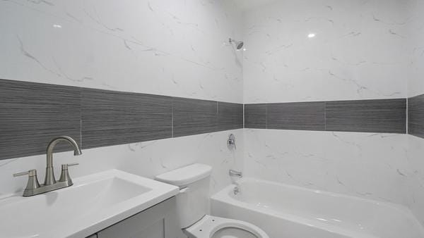 bathroom with tile walls, toilet, vanity, and a bathtub