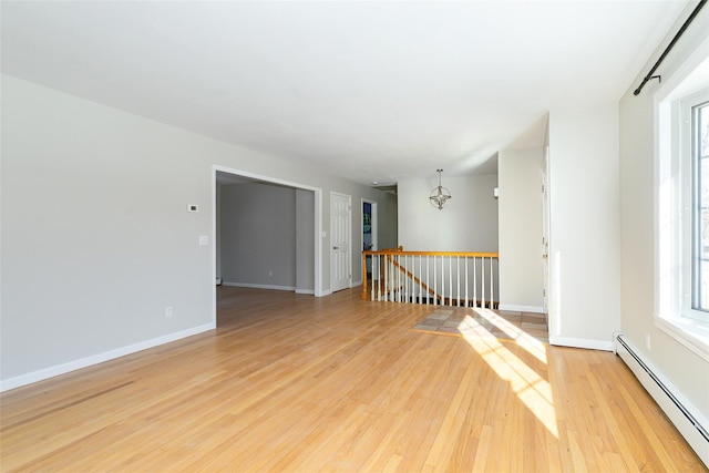 spare room with light hardwood / wood-style flooring, baseboard heating, and a notable chandelier