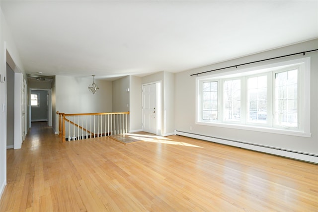 unfurnished room featuring light wood-type flooring, baseboard heating, and a chandelier