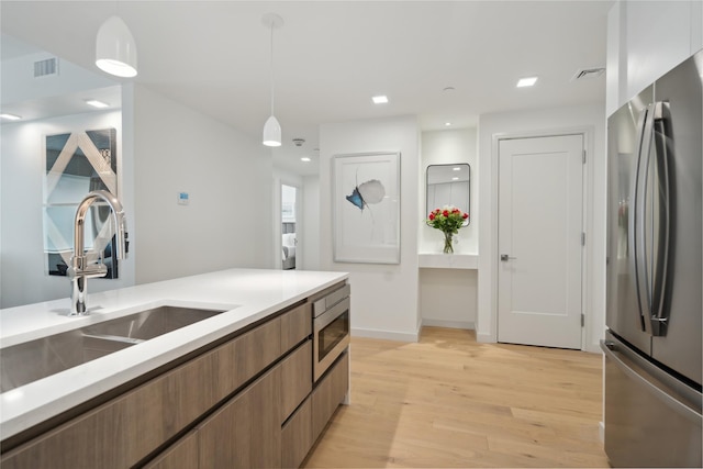 kitchen with light hardwood / wood-style floors, pendant lighting, stainless steel appliances, and sink