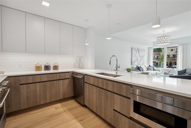 kitchen with light wood-type flooring, sink, dishwasher, white cabinetry, and hanging light fixtures