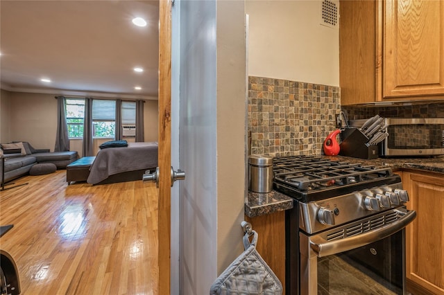 kitchen featuring backsplash, dark stone countertops, light wood-type flooring, high end range, and ornamental molding