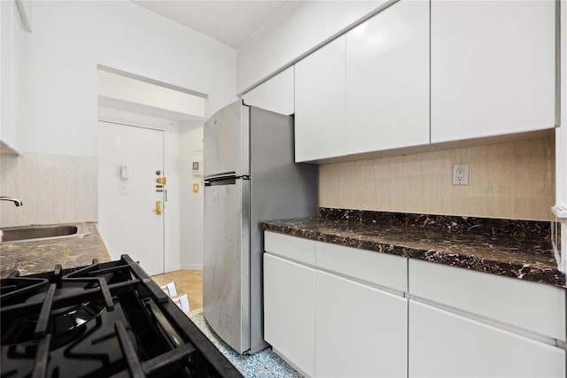 kitchen featuring decorative backsplash, dark stone counters, sink, white cabinets, and stainless steel refrigerator