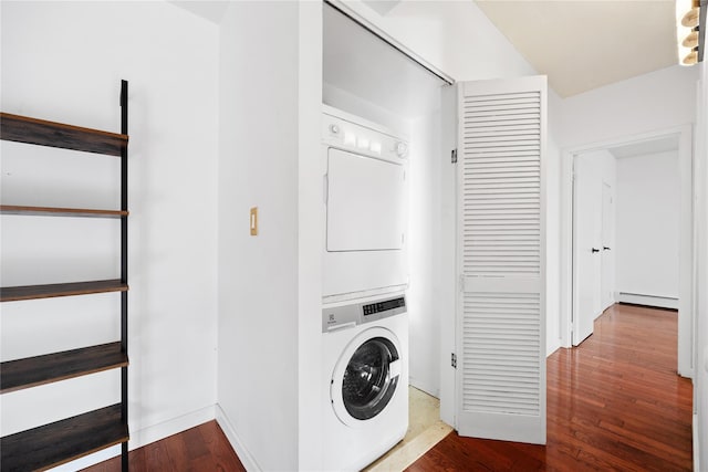 laundry room featuring hardwood / wood-style floors, stacked washing maching and dryer, and a baseboard heating unit