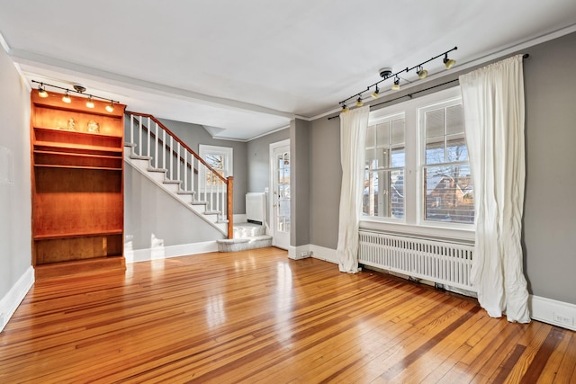 unfurnished living room featuring hardwood / wood-style floors, radiator heating unit, and crown molding