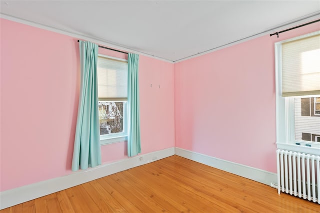 empty room featuring hardwood / wood-style flooring, radiator, and ornamental molding