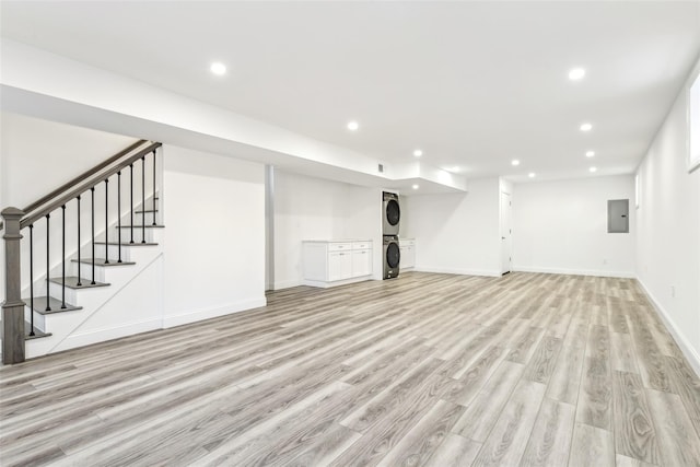 basement featuring light wood-type flooring, electric panel, and stacked washer and dryer