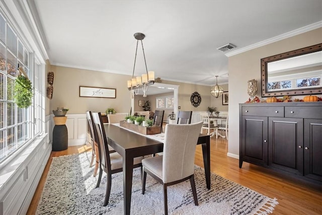 dining area with light hardwood / wood-style flooring, ornamental molding, and a notable chandelier