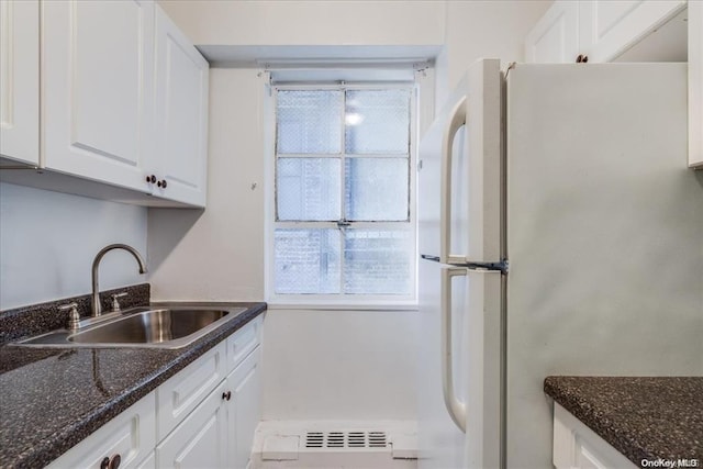 kitchen featuring white fridge, sink, dark stone counters, and white cabinetry