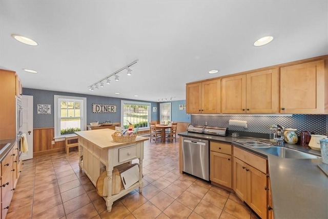 kitchen featuring light brown cabinetry, stainless steel dishwasher, wood walls, and sink