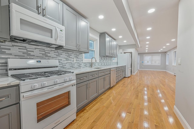 kitchen featuring tasteful backsplash, gray cabinets, light stone countertops, and white appliances