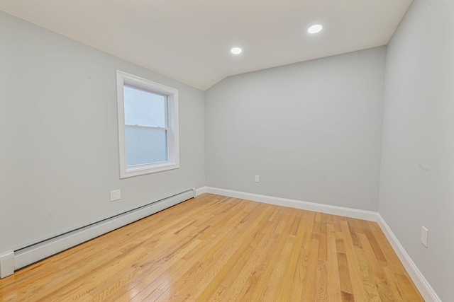 spare room with baseboard heating, light hardwood / wood-style floors, and vaulted ceiling