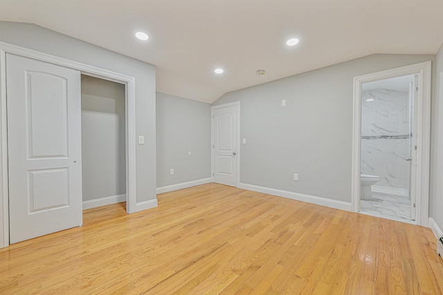 unfurnished bedroom featuring ensuite bathroom, light hardwood / wood-style flooring, and lofted ceiling