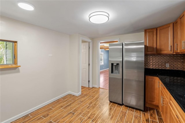 kitchen featuring backsplash, stainless steel refrigerator with ice dispenser, and dark stone counters