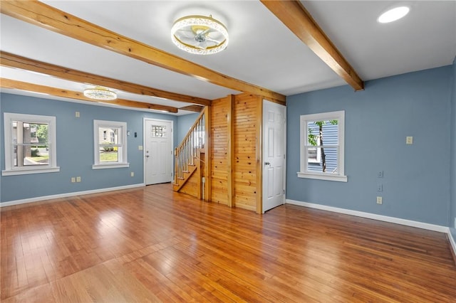 spare room featuring beam ceiling, plenty of natural light, wood walls, and hardwood / wood-style floors