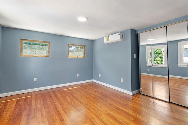 unfurnished bedroom with an AC wall unit, a closet, and light hardwood / wood-style flooring