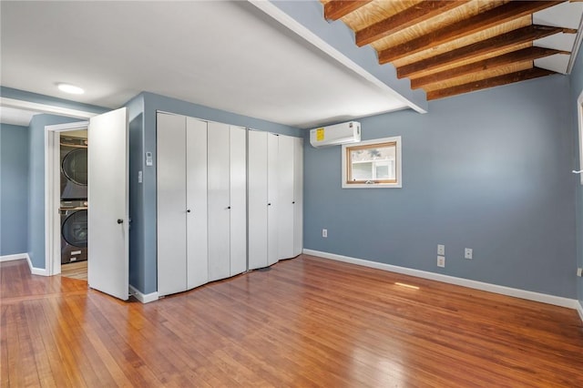 unfurnished bedroom featuring beamed ceiling, stacked washer and dryer, light hardwood / wood-style flooring, and brick ceiling