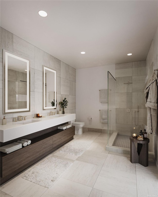 bathroom with vanity, toilet, a shower with door, and tile walls