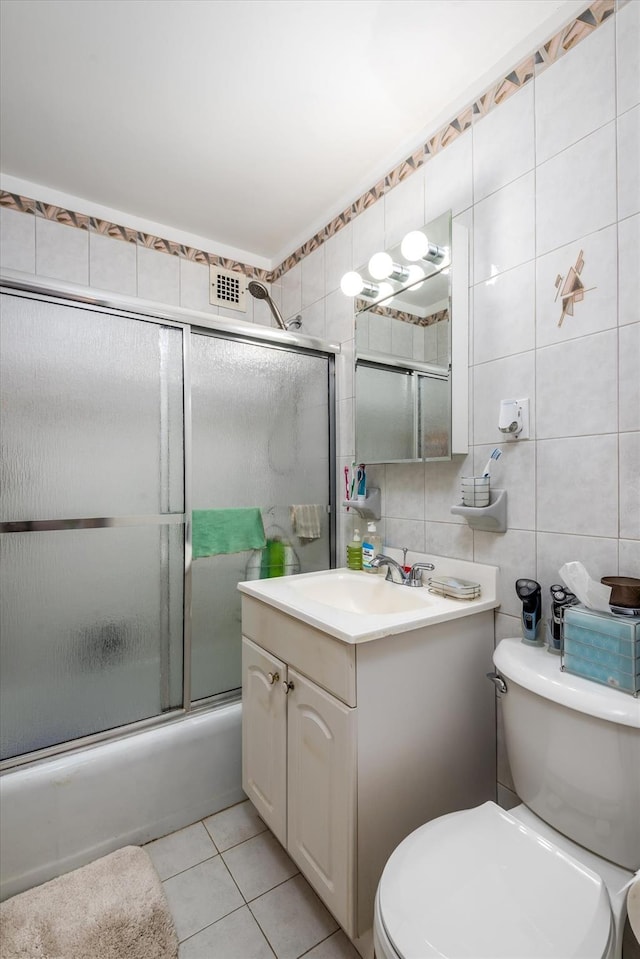 full bathroom featuring vanity, shower / bath combination with glass door, tile walls, tile patterned flooring, and toilet