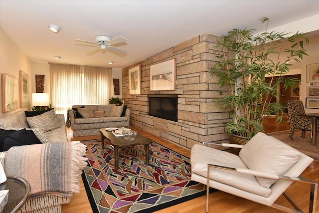 living room featuring ceiling fan, a stone fireplace, and light wood-type flooring