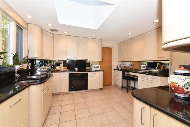 kitchen with a skylight, dark stone counters, sink, light tile patterned floors, and black oven