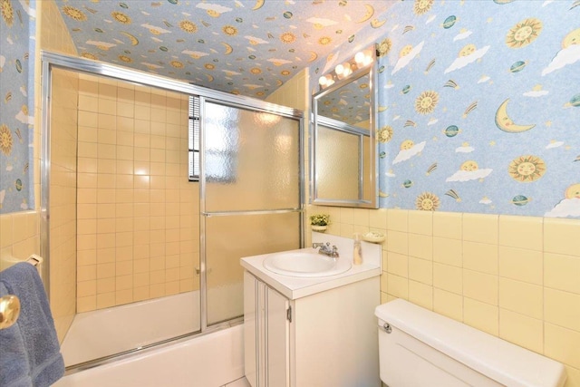 full bathroom featuring combined bath / shower with glass door, toilet, tile walls, and vanity