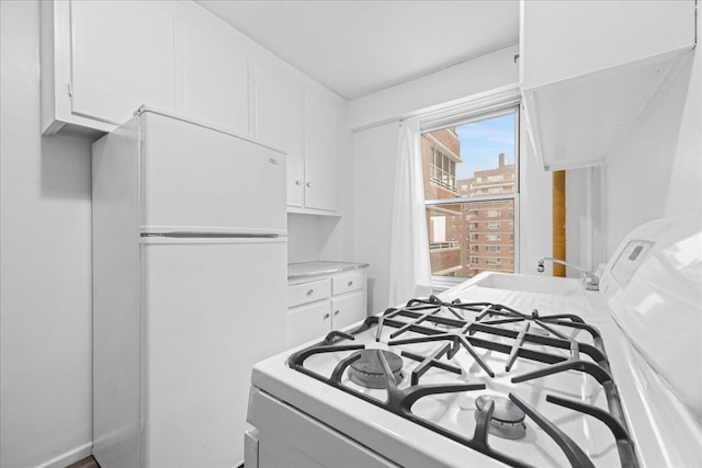 kitchen with white cabinetry, stove, white fridge, and sink