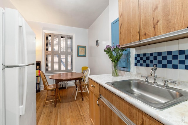 kitchen with tasteful backsplash, sink, light wood-type flooring, and white refrigerator